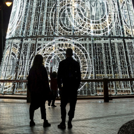 Una pareja y su hijo observan un árbol de navidad iluminado en la Plaza de la Marina, en Málaga.