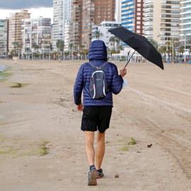Una persona se protege de la lluvia con un paraguas mientras pasea por la playa de Levante de Benidorm