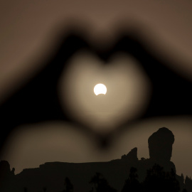 Una mujer hace el gesto del corazón con las manos enmarcando el eclipse de Sol, en el Roque Nublo, en Gran Canaria. REUTERS/Borja Suarez