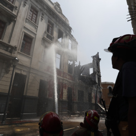Bomberos trabajan en los alrededores de una casona que se incendió ayer durante la jornada de protestas en Lima.