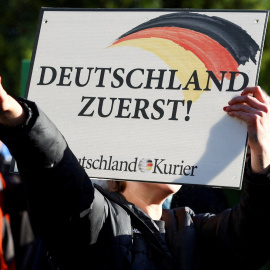 Un seguidor de la formación ultra alemana AfD sujeta una pancarta con el lema "Alemanes primero" y realiza el saludo fascista, en Berlín, a 8 de octubre de 2022.