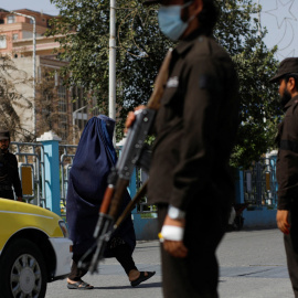 Una mujer afgana camina entre talibanes en un puesto de control en Mazar-i-Sharif, Afganistán, a 6 de agosto de 2023.