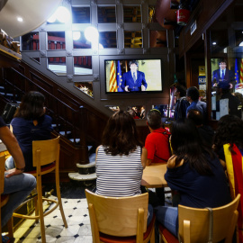 Un grupo de ciudadanos siguen desde una pantalla de televisión la declaración institucional del presidente de la Generalitat, Carles Puigdemont, tras la decisión del Gobierno de aplicar el artículo 155 en Cataluña. EFE/Quique García