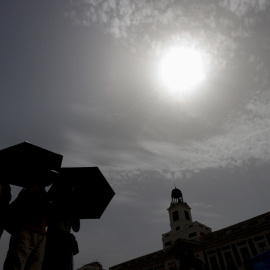 Varios viandantes se protegen del sol mientras cruzan la Puerta del Sol de Madrid.