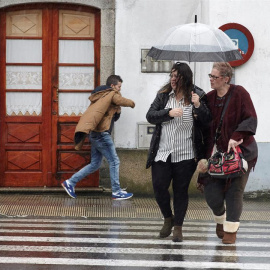Dos mujeres se protegen de la lluvia y el viento mientras cruzan la calle.EFE/Eliseo Trigo
