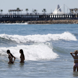 Tres personas se bañan en aguas de la playa del Postiguet en Alacant