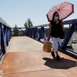 Una mujer se protege del sol con un paraguas mientras cruza por una pasarela.