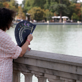 Una mujer combate el calor con un abanico mientras observa el lago del Parque del Retiro de Madrid.