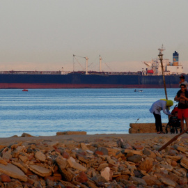 La gente camina por la playa mientras un barco portacontenedores cruza el Golfo de Suez hacia el Mar Rojo antes de ingresar al Canal de Suez.