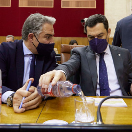 El presidente de la Junta, Juanma Moreno, echa agua en un vaso mientras dialoga con el consejero de Presidencia, Elías Bendodo, este miércoles.