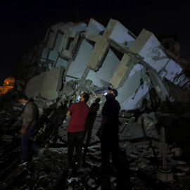 Varios palestinos en el lugar donde un edificio fue destruido por los ataques aéreos israelíes en medio de un estallido de violencia israelí-palestina