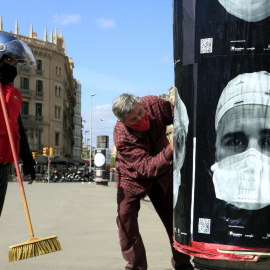 Cartells amb cares de professionals sanitaris amb mascareta en una columna publicitària de plaça de Catalunya de Barcelona, en el projecte 'Behind the mask', que busca el reconeixement col·lectiu davant de la covid-19. 8 d'abril del 2021.