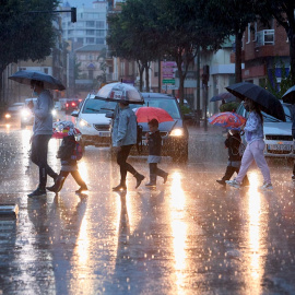 Varias personas cruzan una calle en Valencia bajo la lluvia.