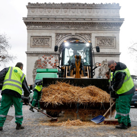 Los trabajadores municipales limpian paja arrojada por un tractor frente al Arco del Triunfo, en París, tras una protesta del sector agrario francés.