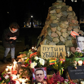 Una mujer se agacha para encender una vela, mientras la gente asiste a un evento conmemorativo, después de la muerte del líder de la oposición rusa Alexei Navalny en Vilna, Lituania.