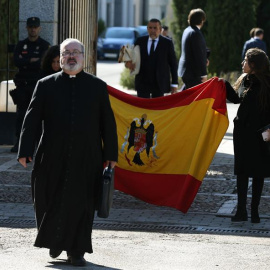 24/10/2019.- El sacerdote Ramón Tejero, que ha oficiado la misa de la reinhumación de Francisco Franco, a su salida del cementerio de Mingorrubio junto a dos familiares del dictador que portan una bandera española con el escudo franquista, tras enterra