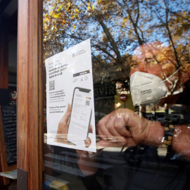 El responsable de un bar del barrio de Gracia de Barcelona cuelga un cartel avisando a sus clientes de la necesidad de presentar el certificado de vacunación para entrar en el local.