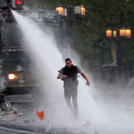 Un manifestante huye del chorro de agua lanzado por la policía durante una nueva jornada de protestas contra el Gobierno del presidente chileno Eduardo Piñera este sábado, en Santiago (Chile). El alza en el precio del pasaje del metro de Santiago prend