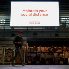 6/07/2021. Imagen de archivo de un hombre caminando bajo un mensaje de salud pública, en Sídney (Australia). - REUTERS