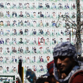 Los yemeníes se paran frente a una enorme pancarta que muestra los retratos de los combatientes hutíes presuntamente asesinados en el conflicto en curso, en una calle antes del séptimo aniversario de la campaña militar dirigida por Arabia Saudita en Y