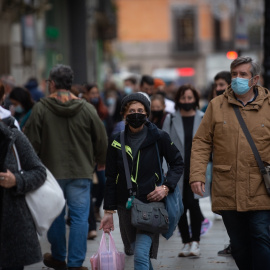 Viandantes caminan con bolsas por una vía de Barcelona, a 27 de diciembre de 2021.