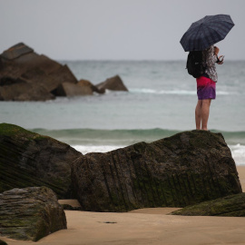 Un joven se protege con un paraguas en la playa de la Zurriola de San Sebastián.