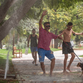Varias personas se refrescan en una boca de riego en un jardín de Murcia.