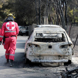 Miembros de la Cruz Roja caminan junto a un vehículo calcinado en una zona afectada por los incendios en Argyra Akti, en Mati. (PANTELIS SAITAS | EFE)