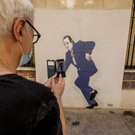 Un hombre hace una fotografía con su móvil al graffiti del rey emérito Juan Carlos I tropezando y a punto de caer, obra pintada en una céntrica calle de Valencia por el artista gallego apodado 'el Primo de Banksy', en Valencia, Comunidad Valenciana (E