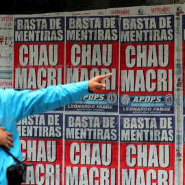 Un agente de Policía da indicaciones a un hombre en el distrito financiero de Buenos Aires junto a un cartel contra Mauricio Macri, el presidente de Argentina. - REUTERS