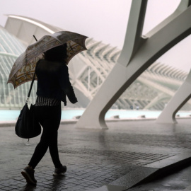 Una mujer se refugia de la lluvia con un paraguas en la Ciudad de las Ciencias de València./EFE
