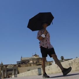 (10/6/2022) Un turista se protege del sol con un paraguas a su paso por el Puente Romano con la Mezquita-Catedral de Córdoba.