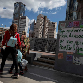 Varias personas caminan frente a un grafiti que dice "La maternidad será deseada o no será aborto legal" en una pared, el 16 de enero de 2021, en Caracas (Venezuela). Una niña de 13 años que era abusada sexualmente por un vecino interrumpió, de maner