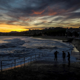 Tres hombres observan la playa de Ondarreta, en San Sebastián, al amanecer. - EFE