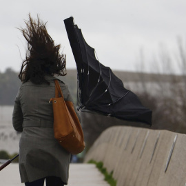 Una mujer sostiene un paraguas que el viento le ha dado la vuelta mientras camina por el Puente Romano de Córdoba