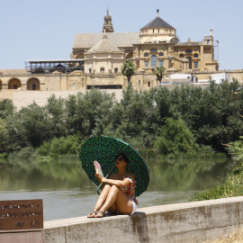 11/07/2022-Una turista se protege del calor con un paraguas y un abanico a la orilla del río Guadalquivir cerca de la Mezquita-Catedral de Córdoba este lunes cuando la Agencia Estatal de Meteorología (Aemet), ha alertado que la segunda ola de calor de 