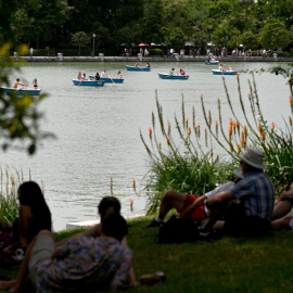 La gente se sienta a la sombra de los árboles mientras otros reman en botes en el Parque del Retiro en el centro de Madrid en la ola de calor de junio de 2022.