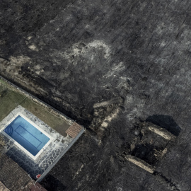 Fotografía tomada con un dron de una piscina y una construcción rodeadas por la superficie calcinada en el pueblo de San Cibrao, Oímbra, Ourense.