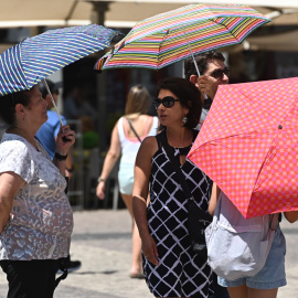 Varias personas caminan con sombrilla por el centro de Madrid.