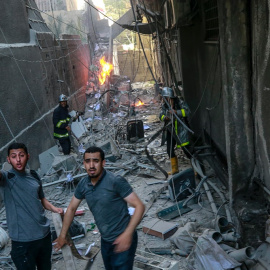 578/22 Dos personas piden ayuda entre los escombros del edificio atacado por el Ejército israelí en Gaza,, mientras un bombero sofoca las llamas