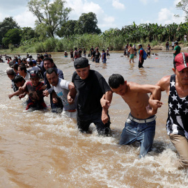 Decenas de personas de la caravana de centroamericanos se unen entre ellas para poder atravesar el río Suchiate, la frontera natural entre Guatemala y México. | Leah Millis / Reuters
