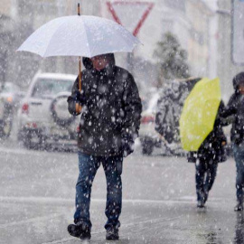 Varias personas caminan bajo una intensa nevada, en la localidad lucense de Piedrafita do Cebreiro ayer lunes. (ELISEO TRIGO | EFE)