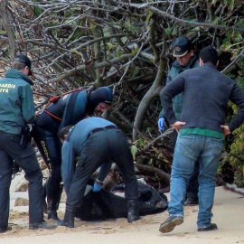 La Guardia Civil junto a uno de los dos cadáveres más hallados de los ocupantes de la patera que naufragó el pasado lunes en la playa de Caños de Meca (Cádiz), mientras que la Policía ha detenido al patrón de la embarcación y a su ayudante, quiene