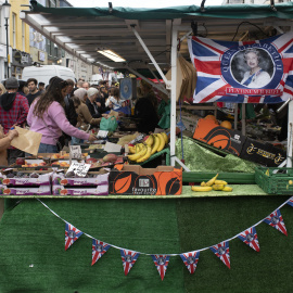 Día de mercado, una mujer mira a la cámara desde un puesto de frutas en la periferia londinense.