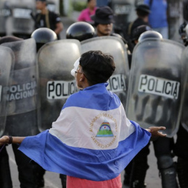 Un joven enmascarado protesta contra el gobierno del presidente nicaragüense, Daniel Ortega, frente a una línea de policías antidisturbios. / AFP - INTI OCON