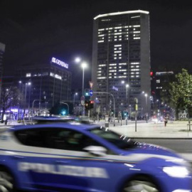A police car patrols in downtown Milan, northern Italy, in front of the Lombardy region headquarters building where office lights have been left on to compose the Italian words 'State a casa' (Stay home), Wednesday, March 18, 2020. Italian authorities say