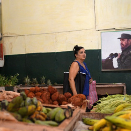 Una mujer compra verduras junto al póster del difunto líder cubano Fidel Castro en un mercado en La Habana. AFP/Yamil Page