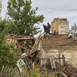 Ciudadanos limpian los escombros de un edificio dañado por los bombardeos en la aldea de Ruski Tyshky del área de Kharkiv.