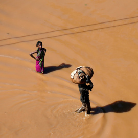 Una niña se detiene para mirar mientras un hombre pasa caminando con el equipaje en la cabeza después del ciclón. Reuters