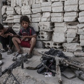Dos niños permanecen en Kobani, Siria, junto a varias armas incautadas a combatientes del Estado Islámico. - AFP